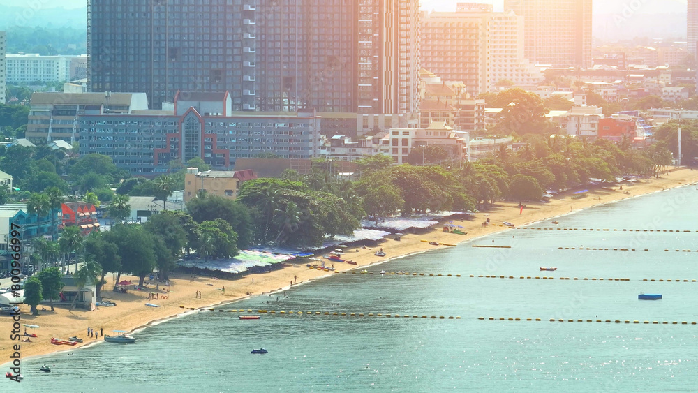 Naklejka premium At sunset, Jomtien Beach bursts with tropical colors, as the sun's fiery embrace meets the azure waters, creating a mesmerizing, postcard-perfect scene. Pattaya, Thailand. Aerial view drone. 