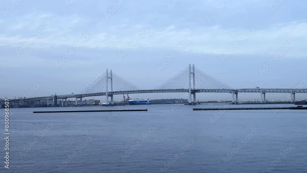 Wide shot of Yokohama Bay Bridge over calm water with cloudy skies, industrial backdrop, serene Wide shot of Yokohama Bay Bridge over calm water with cloudy skies, industrial backdrop, serene