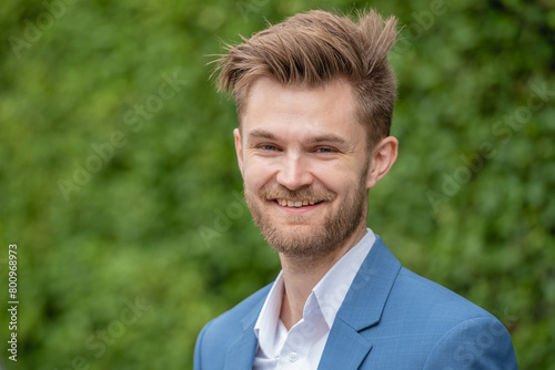 A young professional man wearing a blue suit jacket and white shirt is smiling.