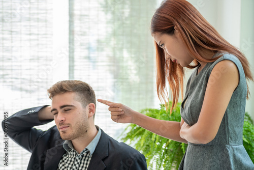 A woman is angrily pointing her finger at a man while he is sitting with his eyes closed and hand on his head.