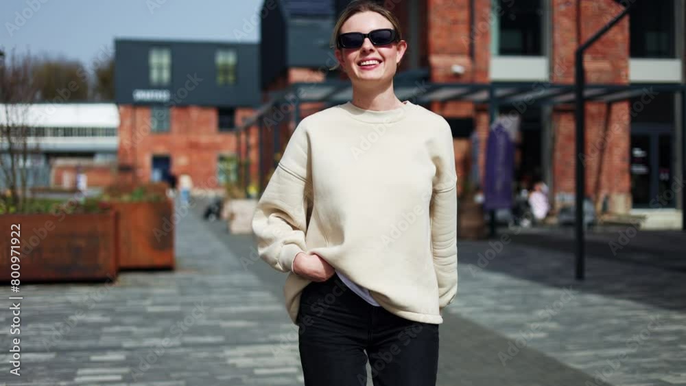 Cheerful female in stylish eyewear calling to follow while actively walking forward along street. Optimistic pretty woman making welcoming hand gesture while smiling and strolling to city building. Cheerful female in stylish eyewear calling to follow while actively walking forward along street. Optimistic pretty woman making welcoming hand gesture while smiling and strolling to city building.