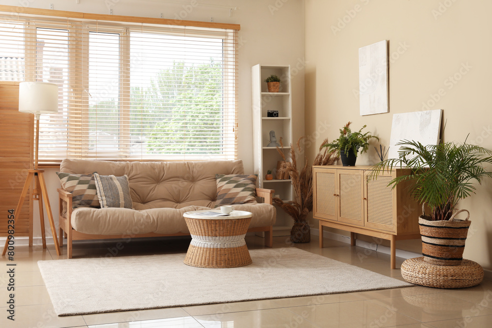 Stylish interior of living room with cozy sofa, chest of drawers, coffee table and houseplants