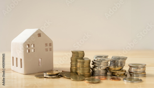 A house model and coins are placed on a wooden table with copy space. Concepts of finance, banking, loans and buying-selling or mortgaging real estate.