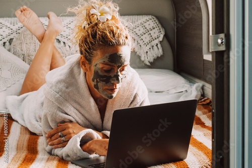 One woman laying on bed inside a camper van in relax leisure indoor activity with skin face cream and working or surfing the web on a laptop computer. Concept of happy lifestyle and travel vanlife