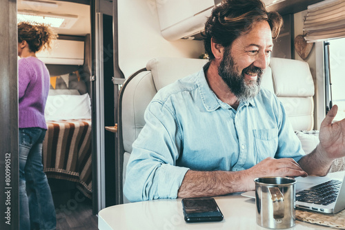 Man and woman living off grid inside a modern camper working on laptop connected online and enjoying freedom and vanlife lifestyle. Happy couple together on travel and vacation. Concept of holiday photo