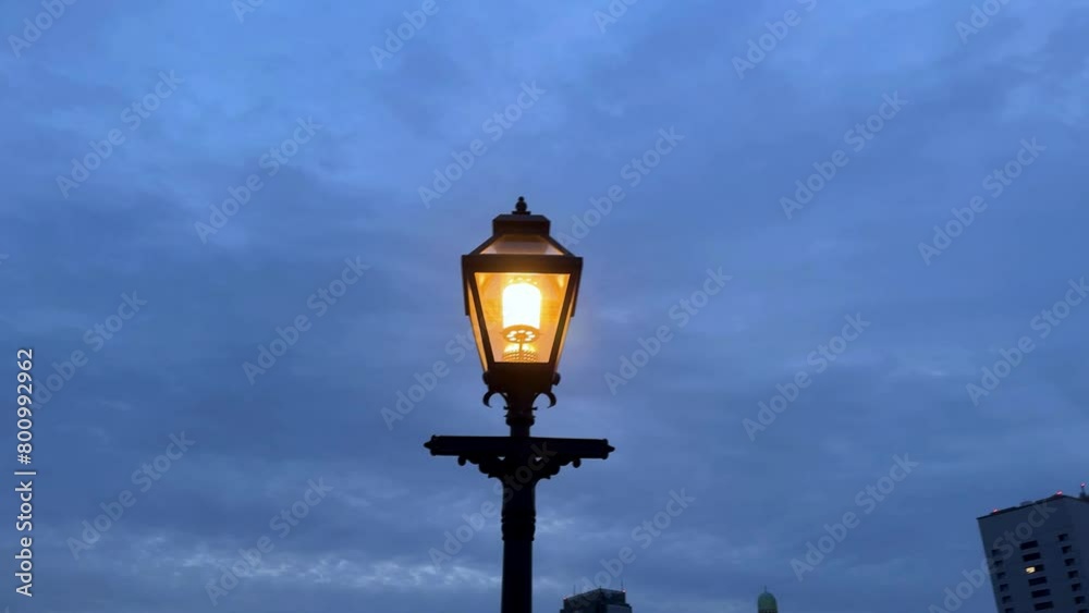 Glowing street lamp against twilight sky, city silhouette in background, peaceful evening atmosphere Glowing street lamp against twilight sky, city silhouette in background, peaceful evening atmosphere