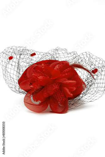 Close-up shot of a red felt pillbox hat with a veil decorated with volume flower, beads and feathers. The hat with an alligator clip is isolated on a white background. Top view.