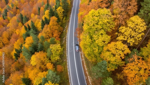 Aerial view over a small road cutting through an autumnal forest
