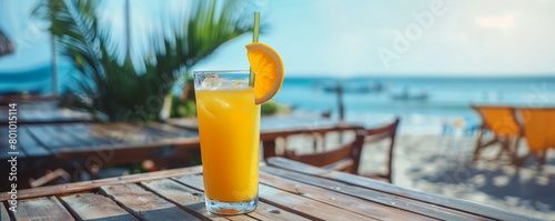 a close-up photo of a glass of orange juice on a chaise longue against the background of a sea beach on a sunny day. Orange cocktail on the beach. advertising a vacation by the sea	 photo