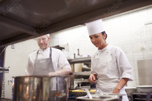 Cooking, chef and trainee in kitchen with pot for food preparation, fine dinning and gourmet cuisine. Professional cook, people and catering in restaurant with ingredients for luxury meal or lunch