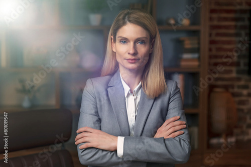 Businesswoman in suit and glasses posing with arms folded, looking at camera and smiling. Female leadership concept