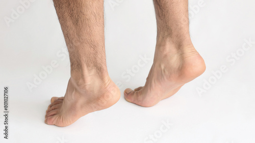 Two male feet standing on tiptoe showing tension in the Achilles tendon, with white background