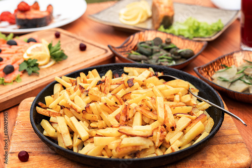 fried potatoes in a golden frying pan on the table serving with salted mushrooms and fish