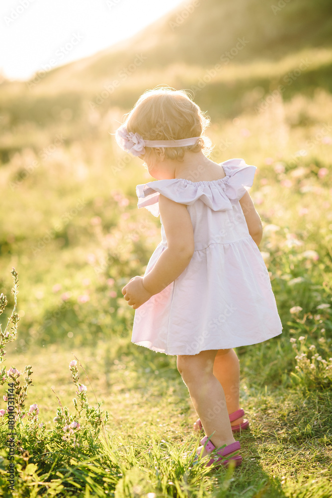 Child running in mountains on summer day. Kid play in spring sunlight outdoors. Toddler walks on green grass in field at sunset. Happy childhood. Beautiful girl walking in nature. Closeup. Back view Child running in mountains on summer day. Kid play in spring sunlight outdoors. Toddler walks on green grass in field at sunset. Happy childhood. Beautiful girl walking in nature. Closeup. Back view