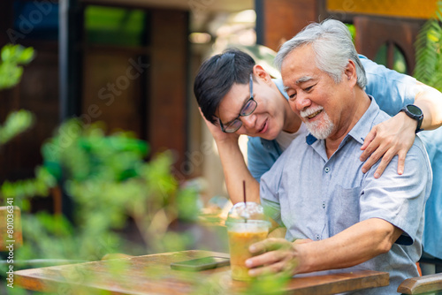 Asian man surprised elderly father with Birthday gift at outdoor cafe restaurant on summer holiday vacation. Family relationship, celebrating father's day and senior people health care concept. photo