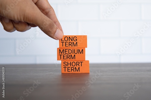 Hand pick wooden cube with text LONG TERM on blue background with copy space. Investment concept. photo