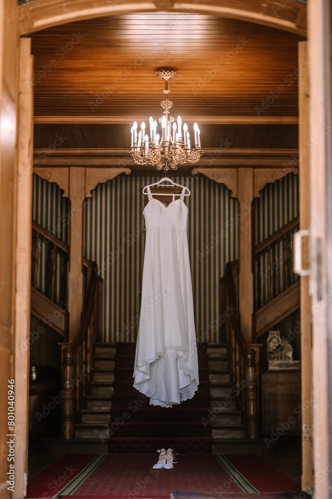 Valmiera, Latvia - August 19, 2023 - A wedding dress hangs from an ornate chandelier in a grand hallway with wooden walls and dual staircases, exuding an air of timeless elegance. Valmiera, Latvia - August 19, 2023 - A wedding dress hangs from an ornate chandelier in a grand hallway with wooden walls and dual staircases, exuding an air of timeless elegance.