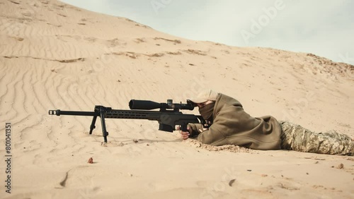 Lying in a prone position, a sniper takes a precise shot amidst an expansive desert, with nothing but the sand and dunes in their scope. Camera 8K RAW. 