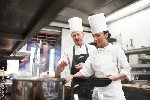 Chef, teamwork and kitchen or pan cooking for hospitality service as preparation, learning or catering. Man, woman and hat at stove for teaching skill for fine dining presentation, recipe or cuisine