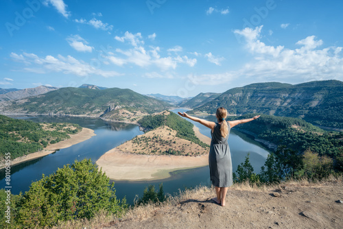 Rear view of a young long-haired woman enjoying the view of one of most picturesque meander of Arda river surounded by mountain slopes of Rhodopi Mountains, Bulgaria. © Jess_Ivanova