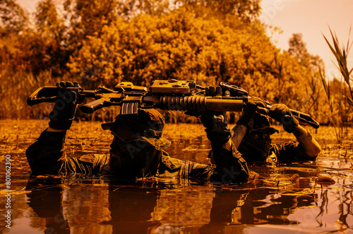 Soldiers move in the heart of a marsh, submerged in swampy waters with only arms and rifle visible, extreme conditions of concealed tactical combat operations of special task forces