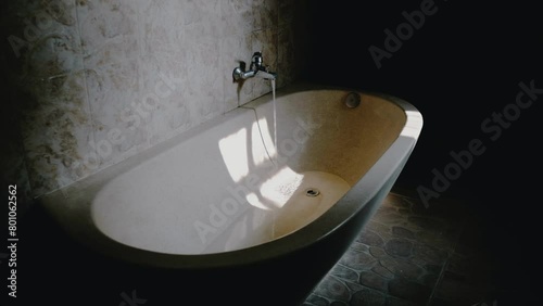 Terrazzo bathtub with a chrome faucet is overflowing with water. Natural light comes from the window. photo