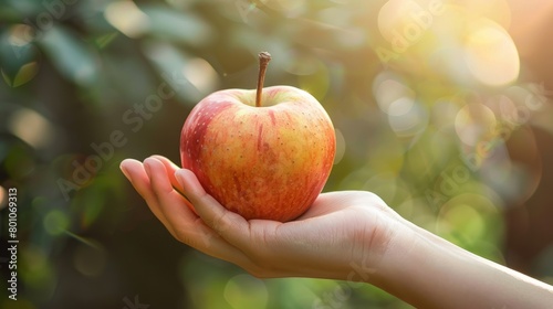 Closeup of a hand holding a vibrant, ripe apple against a blurred background