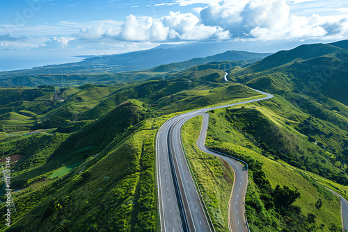 Winding road through lush green hills with expansive sky and distant mountains on a clear sunny day in a scenic landscape