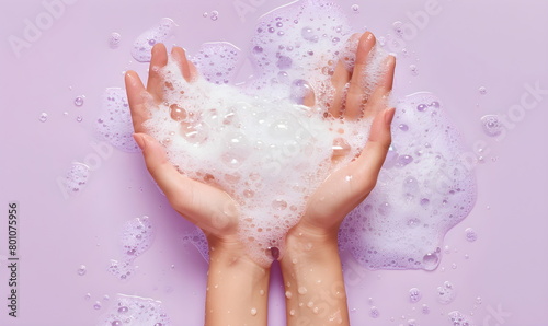 Female hands holding a pile of fluffy white soap foam, concept of hygiene, hand washing and disinfection, top view, on a lilac background