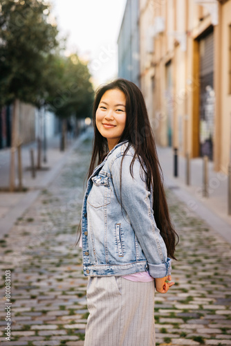 Portrait of a young beautiful smiling asian woman standing on sidewalk of a city street. © Jordi Salas