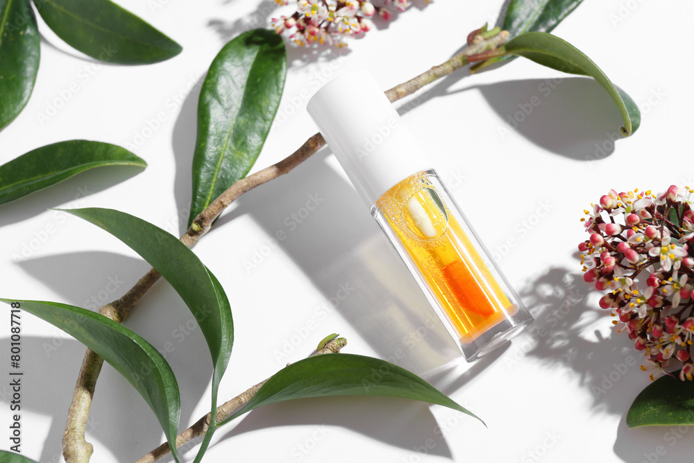 Orange lip gloss, branch, green leaves and flowers on white background, above view Orange lip gloss, branch, green leaves and flowers on white background, above view
