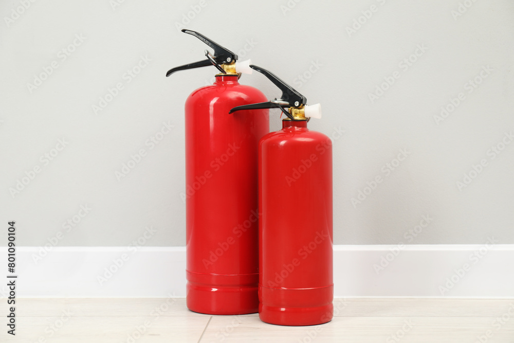 Fire extinguishers on floor near light grey wall Fire extinguishers on floor near light grey wall