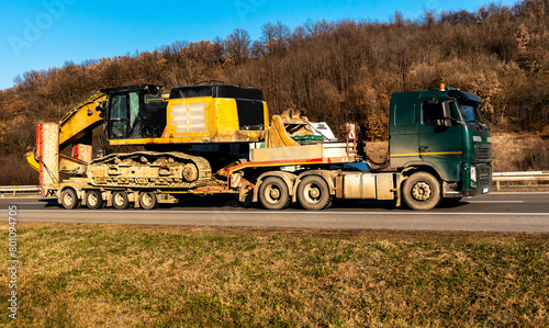 Transportation or Tow Truck carrying Construction Machine Excavator, Backhoe, along the Highway