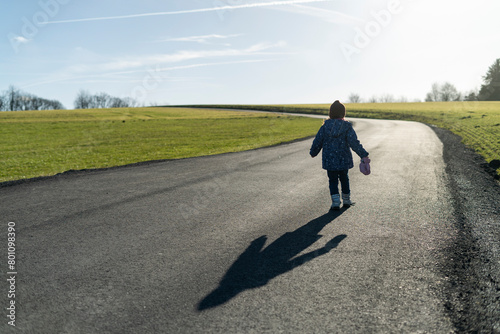 Little girl walking on a road in the countryside with a shadow on the road