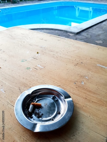 Cigarette butts in ashtray with swimming pool background