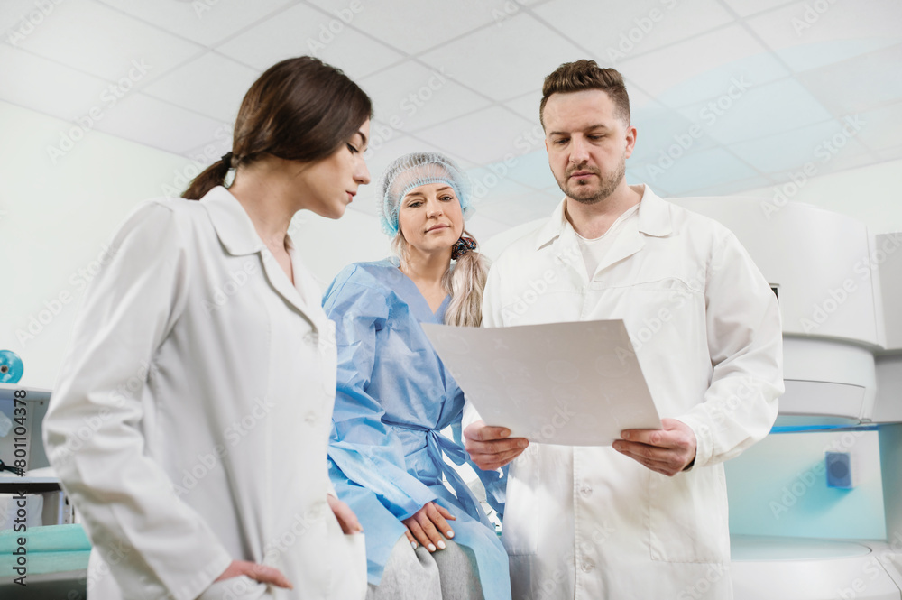 Obraz premium A council of doctors, two people and a mature patient, are studying the MRI result. Postoperative studies. Man doctor and woman doctor looking at MRI scan