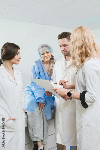A council of doctors of three people and a mature patient are studying the MRI result. Postoperative studies. A man doctor and two woman doctors looking at an MRI scan