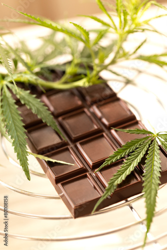Dark chocolate bar placed beside fresh cannabis leaves on a marble background