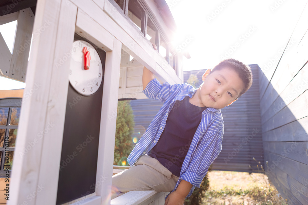 Obraz premium An Asian little boy looks out from a children wooden house. A Korean child is playing in the backyard.