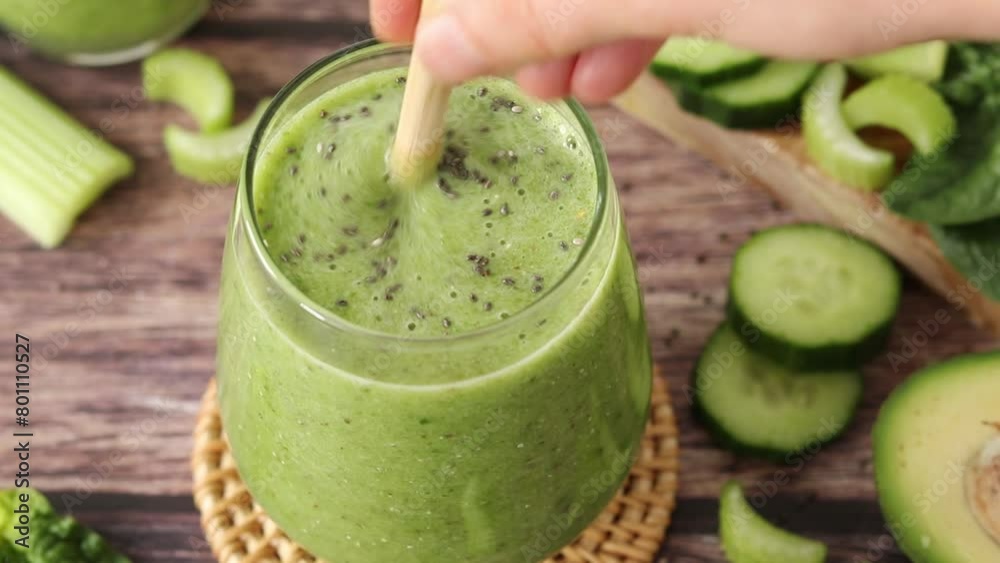 Hand mixing green detox smoothie with chia seeds, cucumber, celery, spinach, and avocado with bamboo straw. Close-up. Healthy blended drink, organic juice, sustainability concept. Hand mixing green detox smoothie with chia seeds, cucumber, celery, spinach, and avocado with bamboo straw. Close-up. Healthy blended drink, organic juice, sustainability concept.
