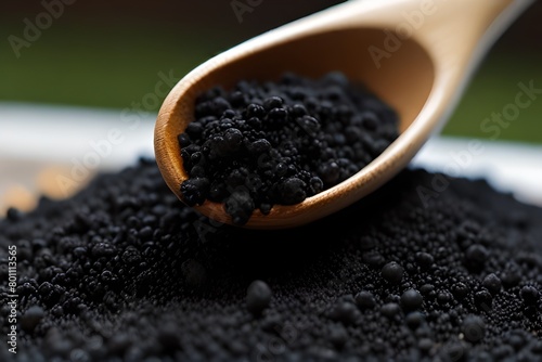 Charcoal in wooden spoon on ground charcoal texture and green background, activated carbon