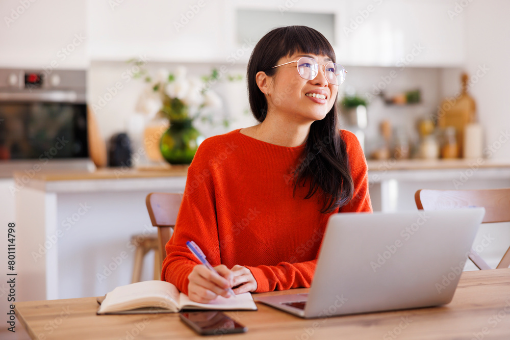 Woman writing notes in planner while taking online course Woman writing notes in planner while taking online course
