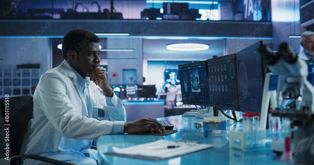 Black Male Neuroscientist Using Desktop Computer To Analyze MRI Scans Of Brain In Medical Research Center Laboratory. African American Surgeon Studying CT Scan Of Patient Suffering From Brain Tumor. Black Male Neuroscientist Using Desktop Computer To Analyze MRI Scans Of Brain In Medical Research Center Laboratory. African American Surgeon Studying CT Scan Of Patient Suffering From Brain Tumor.