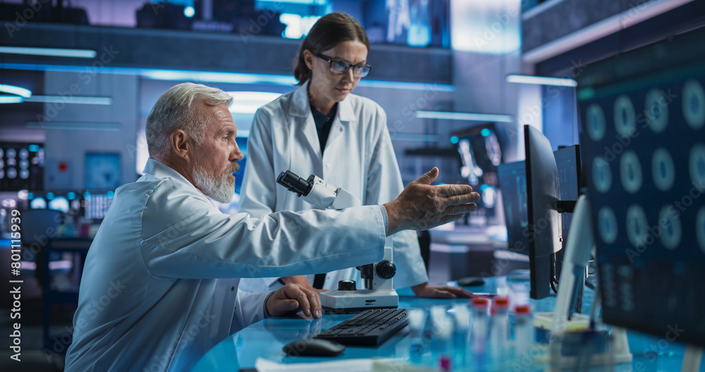 Caucasian Male Neuroscientist Using Microscope to Analyze Petri Dish Sample And Talking To Female Docor In Medical Research Center. Colleagues Discussing Development Of Innovative Mental Disorder Drug Caucasian Male Neuroscientist Using Microscope to Analyze Petri Dish Sample And Talking To Female Docor In Medical Research Center. Colleagues Discussing Development Of Innovative Mental Disorder Drug
