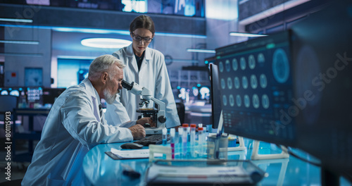 Caucasian Male Neuroscientist Using Microscope to Analyze Petri Dish Sample And Talking To Female Docor In Medical Research Center. Colleagues Discussing Development Of Innovative Mental Disorder Drug photo