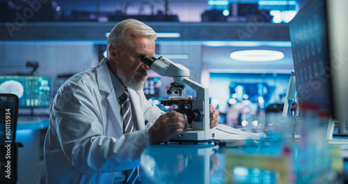 Medical Development Laboratory: Senior Caucasian Male Scientist Using Microscope, Analyzes Petri Dish Sample. Big Pharmaceutical Lab Conducting Biotechnology Research, Developing Innovative Drugs. photo