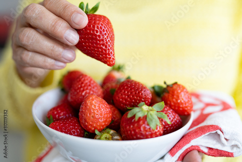 Close-up on senior woman s hand holding a bowl of red fresh ripe strawberries. Healthy eating concept