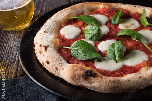 Sliced ​​margherita pizza with basil on a black plate. Side view, close up.