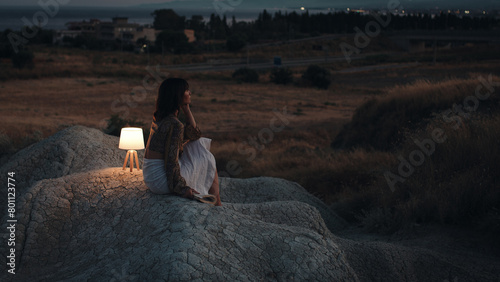 Girl thinks about the future from a rock at sunset with lamp