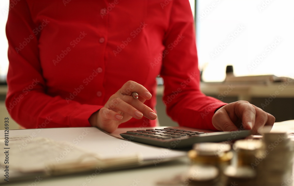 Fototapeta premium Focus on woman hand holding pen and taping calculator. Accountant sitting at table with papers and making business plan. Female accounting income or savings in office